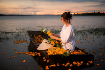 Young woman on a boat with yellow flowers in the lake during the sunset © Wosunan