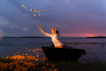 Young woman on a boat with yellow flowers in the lake during the sunset © Wosunan