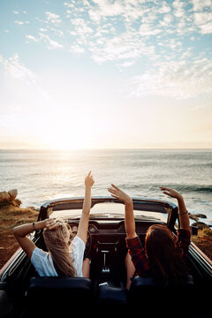 People, friends and celebration in convertible by beach for adventure, freedom and holiday with music. Back of driver and passenger with arms up for success, carefree and vibing in car by sunset