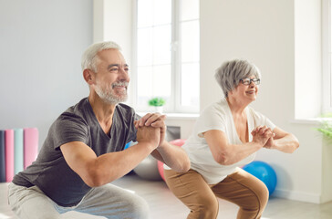 Obraz premium Smiling mature senior man and woman doing sport stretching exercises standing in gym indoor. Happy elderly people doing workout in rehabilitation center for health. Fitness in retirement concept.