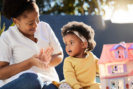 Mother, baby and playing with toy in garden of home with doll house, fantasy and clapping hands with game. Black people, mom and daughter in backyard outdoor with bonding, support and imagination