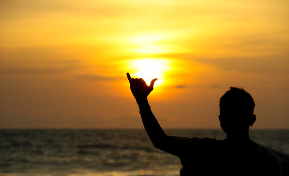 A surfer holds up a cowabunga sign in front of a beach sunset on Kuta beach in Bali Indonesia