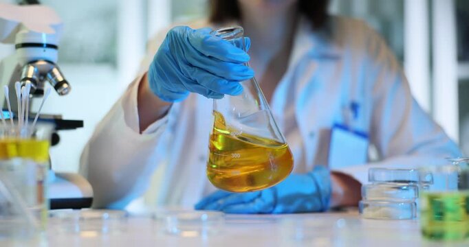 Laboratory worker shakes beaker with yellow oil liquid