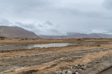 Cold desert landscape from Nubra Valley in Ladakh, India. Sand roads and dry vegetation. Scenic view of Himalayas and Ladakh ranges. Beautiful barren hills in Ladakh with dramatic clouds in background