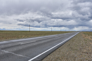 Asphalt road in the steppe of Mongolia under the cloudy sky
