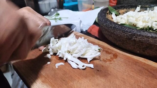 chopping cabbage on a cutting board as one of Lotek's cooking ingredients. Lotek is a salad made from Javanese (Indonesian) vegetables with peanut sauce