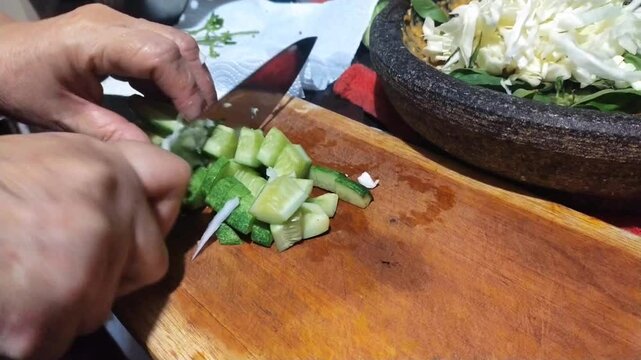 cutting cucumber on a cutting board as one of Lotek's cooking ingredients. Lotek is a salad made from Javanese (Indonesian) vegetables with peanut sauce