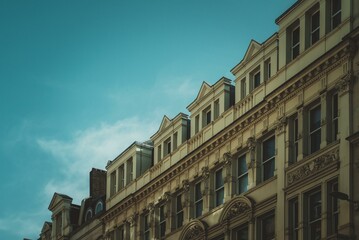 An ornately decorated building in London, UK, with a light blue sky and clouds above.  The building is cream-colored and has many windows.