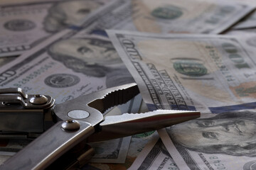 A close-up of metal tongs or pliers grabbing a hundred-dollar bill against a background of hundred-dollar bills, symbolizing the concept of the central bank cutting or tightening interest rates.