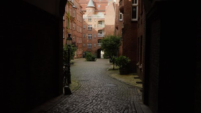 Explore a quaint cobblestone alley opening to picturesque historic buildings. Ideal for travel documentaries or historical features.