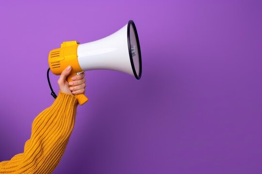 Pink megaphone in hand against purple wall background