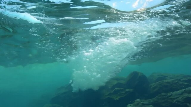 A waterfall from beneath the water surface showing the bubbles and turbulence created by the falling water. The camera captures the underwater environment and the power of the waterfall.