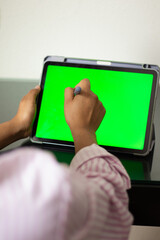 Hands of a woman working on a tablet with a green screen and a digital pen, studying on the desk in the hotel room with an internet connection