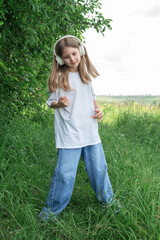 Fototapeta premium A child with headphones listening to music and dancing in the park.