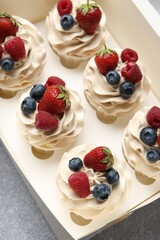 Tasty cupcakes with different berries in box on light grey table, above view