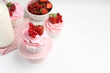 Tasty cupcakes with strawberries and red currants on white table, space for text