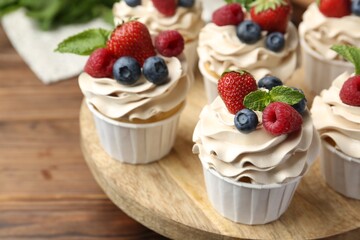 Tasty cupcakes with different berries and mint on wooden table, closeup
