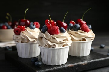 Tasty cupcakes with different berries on black wooden table, closeup