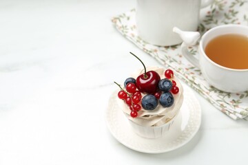 Tasty cupcake with different berries and tea on white marble table, space for text