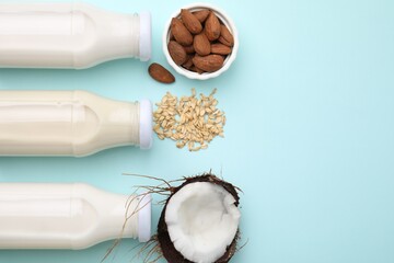 Different types of vegan milk in bottles and ingredients on light blue table, flat lay. Space for...