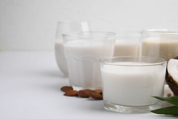 Different types of vegan milk and ingredients on white table, closeup