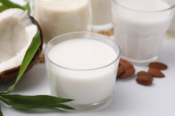Different types of vegan milk and ingredients on white table, closeup