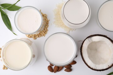 Different types of vegan milk and ingredients on white table, flat lay