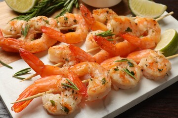 Skewers with delicious grilled shrimps served on wooden table, closeup