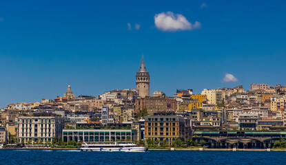 Fototapeta premium A ferry sails in the Bosphorus Strait with the Galata Tower and the Istanbul skyline in the background. A clear blue sky with a few white clouds on a sunny day.
