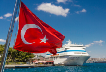 A Turkish flag waves in the breeze against the backdrop of a large cruise ship in Istanbul's harbour. Turkish flag waving in istanbul harbor