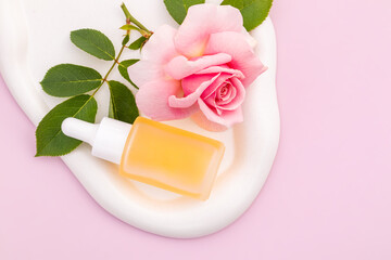 A glass cosmetic dropper bottle with blank label on white ceramic tray with rose flower on pink background. Trendy beauty product design, branding. Mockup cosmetics , copy space