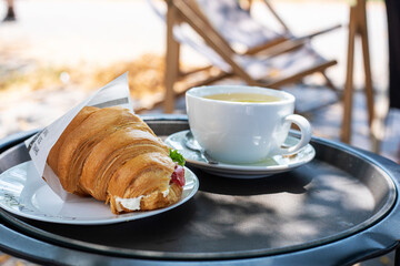 hot delicious croissant with tuna and a cup of ginger tea on the table outside. snack