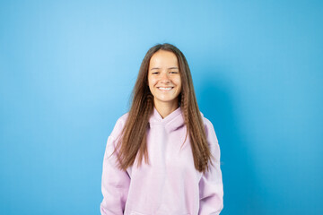 Teenager portrait on blue background, cool student in sweatshirt, young cute emotional teen with smile, curly haired adolescent, stylish fashion