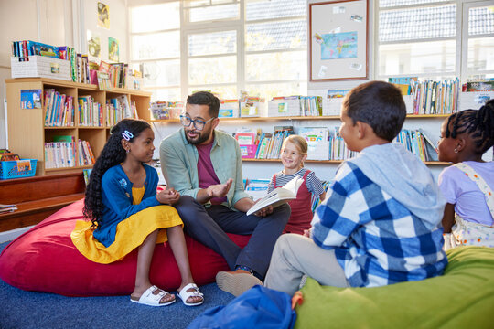 Teacher reading book to his little students in a library