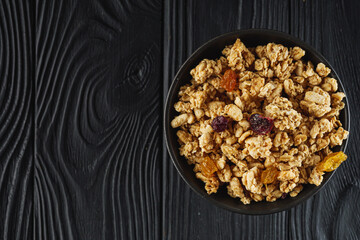 tasty crunchy granola with dried fruits on a black wooden rustic background