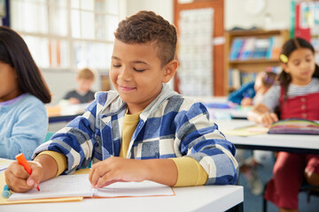 Mixed race school boy writing in primary classroom during test
