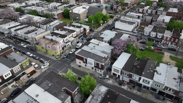 Row of houses in american town during spring season. Rooftops of homes and Buildings in USA. Blossoming trees in dangerous suburbia. Aerial top down.