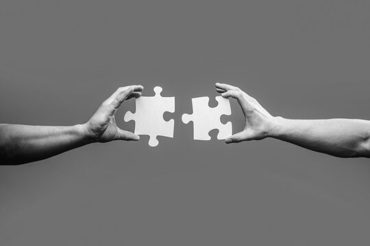 Men holding and putting a piece of jigsaw puzzle together. Two hands trying to connect couple puzzle piece. Black and white