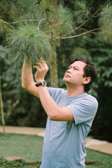 A Southeast Asian man examines lush green leaves in a dense forest, capturing the essence of nature's beauty and biodiversity