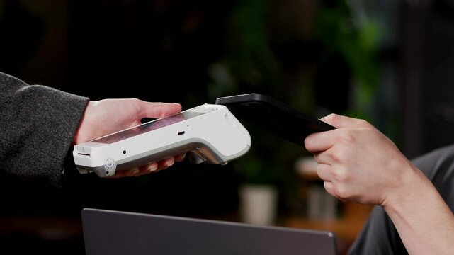 Pays from a contactless mobile phone to a credit card system. Payment by smartphone using wireless systems. Mobile payment concept - young man pays using contactless phone to credit card system.