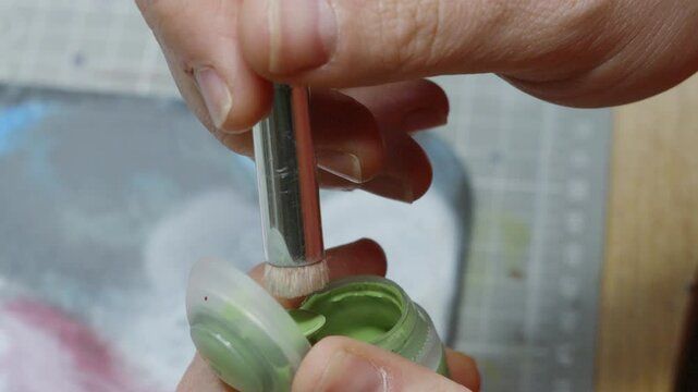 Close Up of Male Hands Opening Green Paint Pot and Dipping Flat Brush Getting Ready to Paint Model