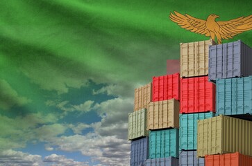 Zambia flag and big stack of shipping cargo containers in docks with sky background close up