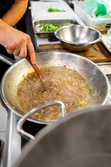 A hand stirs sautéed onions in a pan on a stove, suggesting cooking or meal preparation.