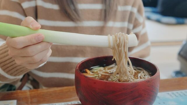 Woman tourist eating Negi Soba or Buckwheat noodles with a raw leek instead of chopsticks, famous soba when visit Ouchi Juku ancient farmer house in Shimogo, Minamiaizu, Fukushima Prefecture, Japan