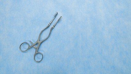 Fototapeta premium A Weitlaner self-retractor used in heart surgery placed on a blue background. Medical instruments used in the operating room. Surgical clamp with retainer.