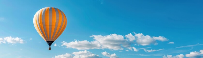 Obraz premium A colorful hot air balloon floating in a clear blue sky with scattered clouds, exemplifying adventure and freedom in a serene landscape.