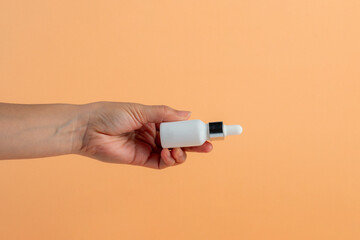 White glass cosmetic bottle in hand, Skin care or sunscreen cosmetic on cream background.
