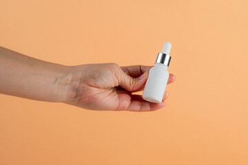 White glass cosmetic bottle in hand, Skin care or sunscreen cosmetic on cream background.