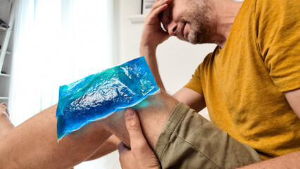 Man with painful knee and leg injury at home cooling down with ice pack..