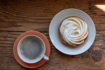 Traditional french lemon tart with meringue and coffee cup with espresso on the rustic wooden windowsill